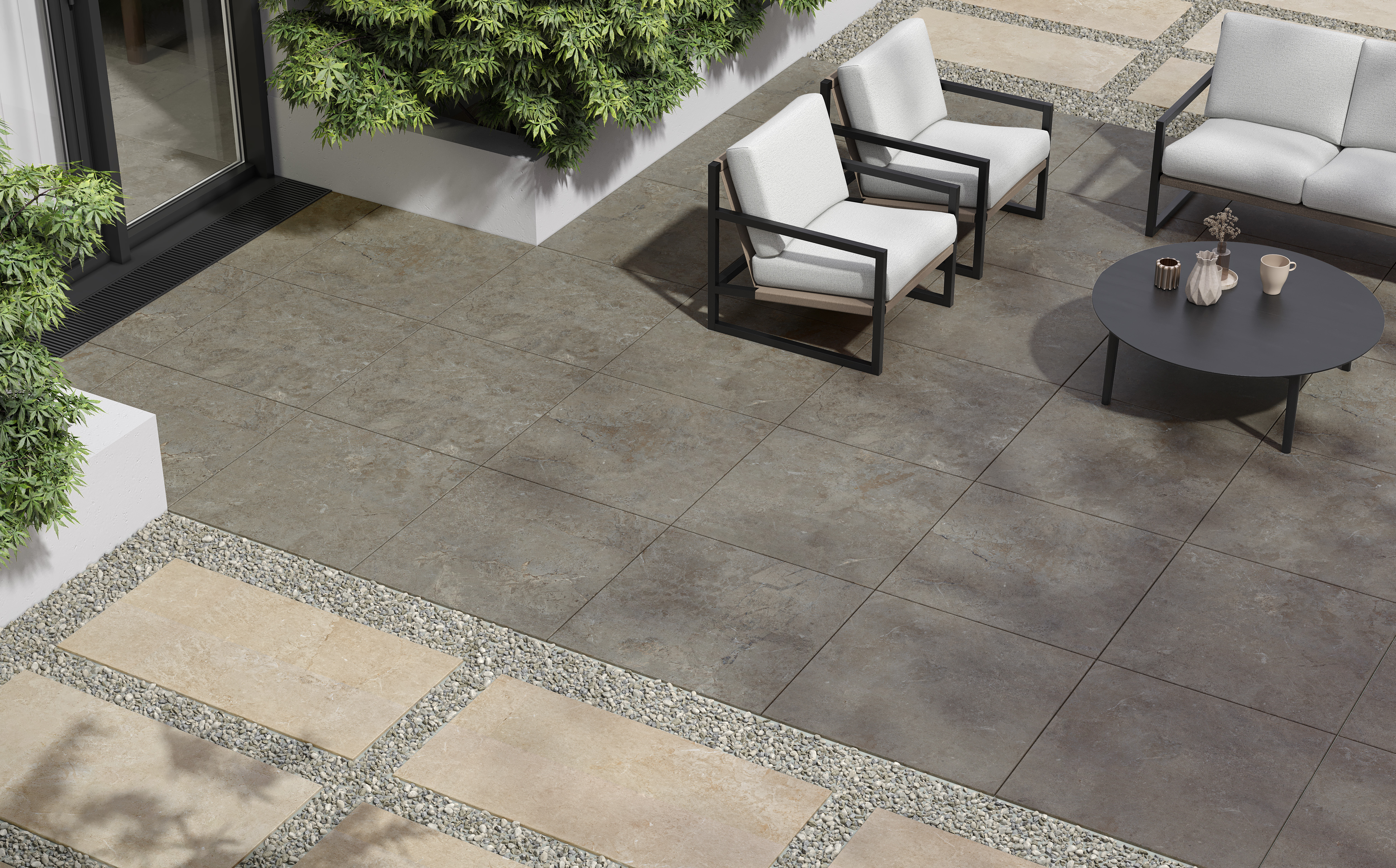 Moderne Outdoor-Terrasse mit großformatigen, quadratischen Feinsteinzeugfliesen in natürlichem Grauton. Die Fliesen haben eine feine, steinähnliche Struktur und sind im Format 60 x 60 cm verlegt. Sie wirken robust, rutschfest und sind ideal für den Außenbereich geeignet. Im Hintergrund ist eine gemütliche Sitzgruppe mit hellem Polster und ein runder, schwarzer Tisch zu sehen, eingerahmt von grünen Pflanzen und beige-grauen Fliesen im Kiesbett.