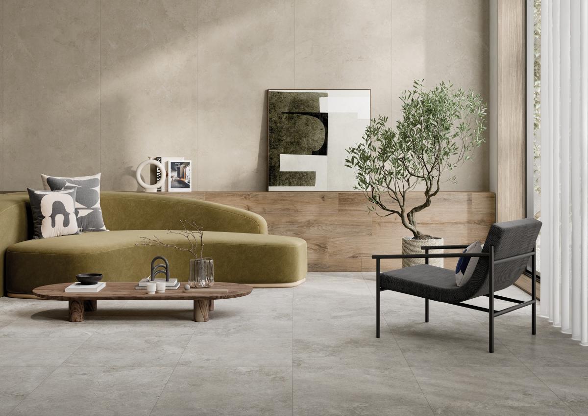 Ein stilvoll eingerichtetes, modernes Wohnzimmer mit einem olivgrünen Sofa. Davor steht ein ovaler Couchtisch aus Holz. Rechts im Bild befindet sich ein schwarzer Sessel. Die Wand ist teils mit beige-grauen Steinfliesen, der Boden mit oßformatigen, hellgrauen Feinsteinzeugfliesen ausgelegt.