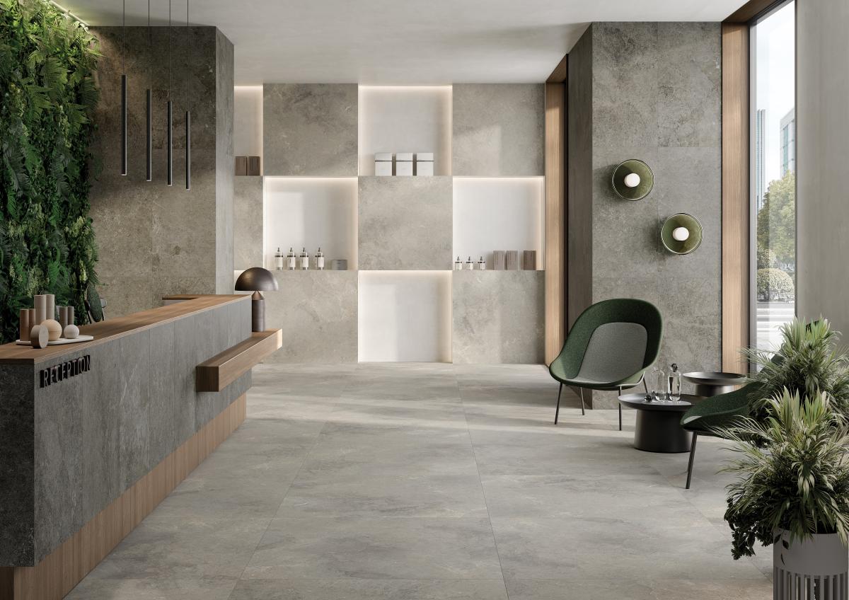 Ein modern gestalteten Empfangsbereich mit einem eleganten, minimalistischen Design. Der Raum ist geprägt von großformatigen Boden- und Wandfliesen aus der Serie Baltico, die in natürlichen Grautönen gehalten sind. Die Fliesen zeichnen sich durch ihre matte Oberfläche und ihre natürliche Steinoptik aus, die dem Raum eine ruhige und edle Atmosphäre verleihen.  Die hochwertigen Fliesen verlaufen nahtlos vom Boden bis zu einzelnen Wandflächen und schaffen ein harmonisches Gesamtbild.
