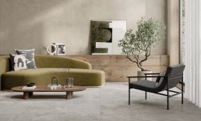 Ein stilvoll eingerichtetes, modernes Wohnzimmer mit einem olivgrünen Sofa. Davor steht ein ovaler Couchtisch aus Holz. Rechts im Bild befindet sich ein schwarzer Sessel. Die Wand ist teils mit beige-grauen Steinfliesen, der Boden mit oßformatigen, hellgrauen Feinsteinzeugfliesen ausgelegt.
