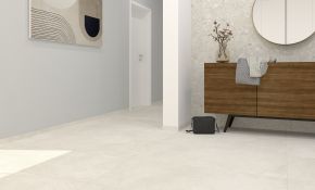 Ein modern gestalteter, heller Flur- und Eingangsbereich mit großformatigen, beigefarbenen Bodenfliesen, einer hellblauen Wand mit einem abstrakten Kunstwerk und einer gegenüberliegenden Wand in Terrazzo-Optik, vor der ein Sideboard aus dunklem Holz steht.