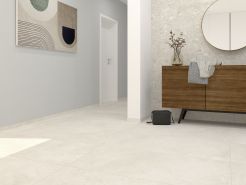 Ein modern gestalteter, heller Flur- und Eingangsbereich mit großformatigen, beigefarbenen Bodenfliesen, einer hellblauen Wand mit einem abstrakten Kunstwerk und einer gegenüberliegenden Wand in Terrazzo-Optik, vor der ein Sideboard aus dunklem Holz steht.